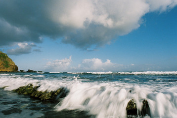 Wave crashes into tidal pool beneath azure Caribbean sky