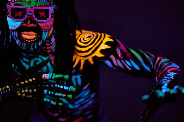 portrait of cool african man with fluorescent body art dancing isolated in dark space. dj man perform dance, mysterious dancer with colorful prints on face and body