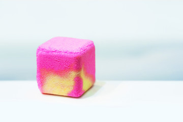 Salt bath bomb. Pink and yellow cube of bath salt lies on the bath