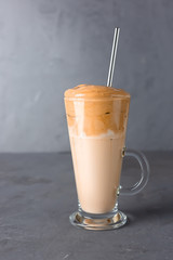 Korean iced Dalgona coffee in tall glass on a grey table. Trendy fluffy creamy whipped coffee