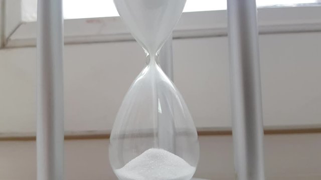 Hourglass with sand on the window background, symbol of the passage of time, 4K video