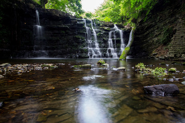 Obraz premium Hidden gorge with a large waterfall with smooth flowing water