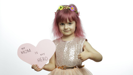 Child girl princess holds pink paper heart with text about mother. Mother's day