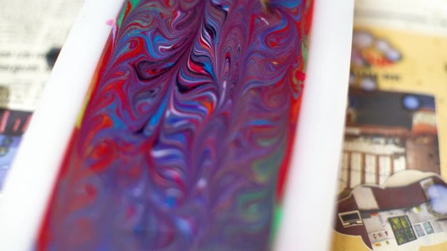 Soap artisan using a long wooden stick skewer to create colorful swirls into a liquid soap in a white silicon mold before it sets to make a soap loaf