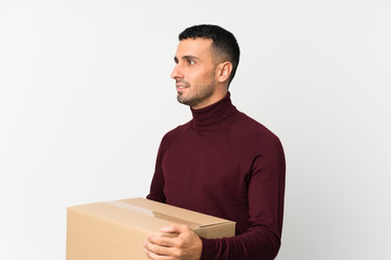 Young man over isolated white background holding a box to move it to another site