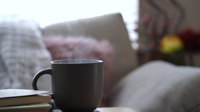 Hot coffee or tea with steam on table with blurry cushions on sofa background, Scene cozy and relaxing at afternoon break in sunny day on spring or summer, English traditional 