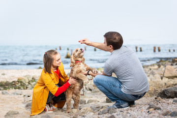 Young couple playing with a dog on a sea coast. Dog walking outdoors.