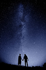 Fototapeta na wymiar Couple is standing in mountains against night sky with milky way
