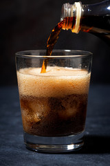 Coca Cola is pouring into a glass from a bottle, vertical