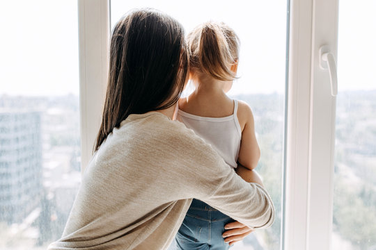 Mother and daughter looking through the window to empty city.