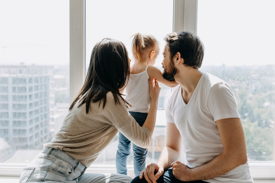 Family of three, father, mother and daughter looking through the window to empty city.