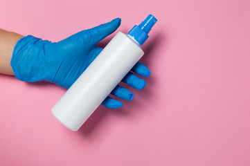 Coronavirus protection. Hand in blue disposable glove holding surface disinfectant or hand sanitizer dispenser on pink background. Hygiene measures to prevent spread of Covid-19 pandemic