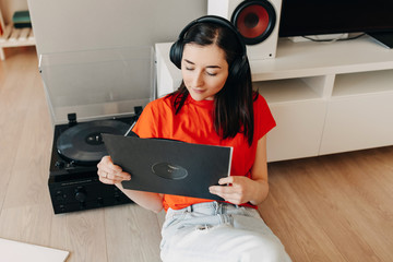Close-up portrait if a young brunette woman wearing red t-shirt, sitting on the floor, listening to...