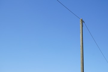 A single high voltage power line against blue cloudless sky. Overhead line on a wood pylon.