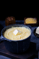 Corn porridge with milk in a black saucepan against the dark background