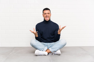 Young handsome man sitting on the floor unhappy and frustrated with something