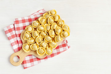 tortelloni  on a wooden board over red checked tablecloth. copy space