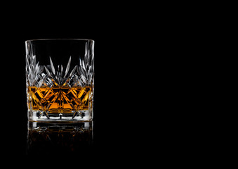 Scotch whiskey in crystal elegant glass on black background with reflection.