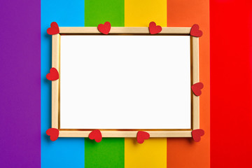 wooden frame with blank white copy space for text on multicolored rainbow flag background and little red hearts.