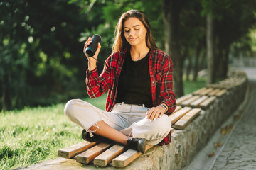 Modern trendy girl listening to music by wireless portable speaker.Young beautiful american woman enjoying,dancing in park.