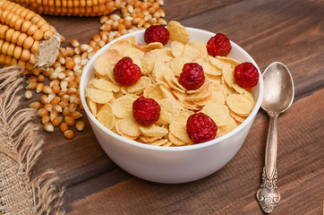 Close-up cornflakes with raspberries and ears of corn on a dark wooden background. Healthy food, breakfast