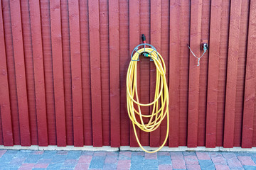 Yellow rubber watering tube for plants watering hangs on red wooden wall of traditional Swedish...