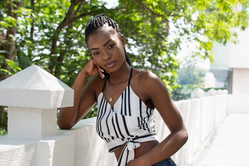 Beautiful African woman leaning on wall and looking at camera. Copy space. Woman wearing striped short top. Vacations, summer concept. Kenya woman. Thoughtful, serious expression.