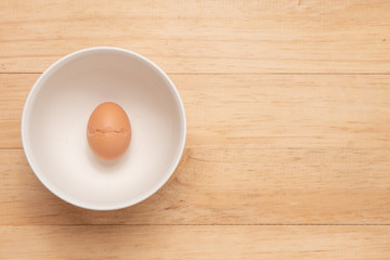 One of broken chicken egg on a white cup place on light brown wooden background, Top view with copy space