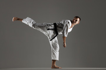 man exercising karate, against gray background, harsh side lit