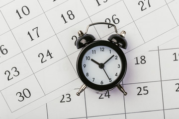 Flat lay or top view of black alarm clock with white calendar on wooden  board with copy space, schedule for vacation, reminder for business appointment