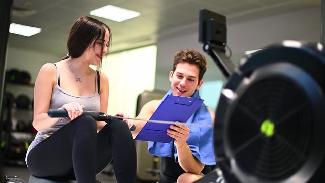 Young woman working out on the rowing machine, personal trainer explaining the technique