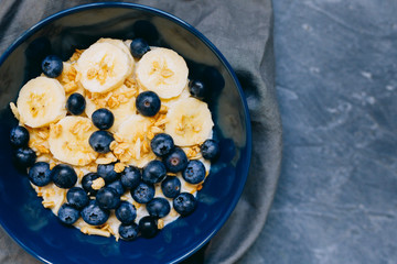 Close up Dark blue bowl of oatmeal porridge with banana and blueberry on vintage table top view in flat lay style. Hot breakfast and homemade food. Free space. Homemade cuisine. 