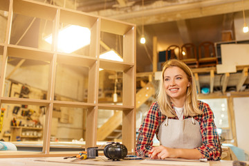 smiling carpenter woman at work, lady has her own workshop of making furniture for customers. professional cutting, drilling and projecting wooden handicraft