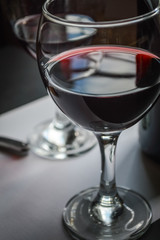 Closeup of glasses of red wine and bottle with shadows and reflections on a white textured surface.