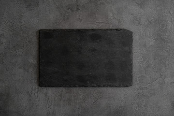 Empty black cutting board of stone on a gray concrete grunge textured background. Copy space