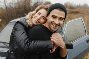 Smiling woman emracing her man from the back at the background of the car