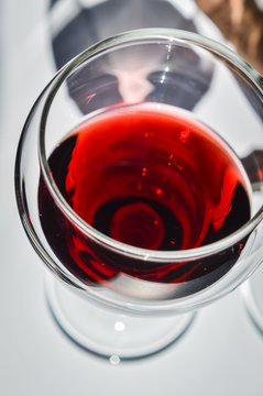 Closeup of  a glass of red wine with shadows and reflections on a white textured surface.