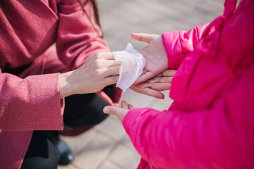 Obraz na płótnie Canvas Mom and daughter walk in the park during quarantine of the coronavirus. Mom rubs her daughter's hands with a napkin. Personal hygiene during the COVID-19 Pandemic