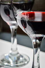 Closeup of glasses of red wine and bottle with shadows and reflections on a white textured surface.