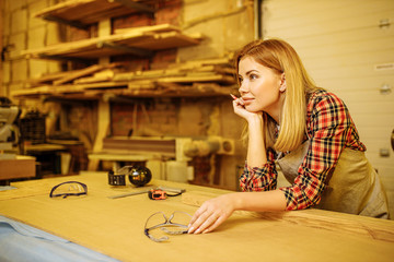 attractive lady woodworker have rest after work in factory. beautiful woman leaned on wooden table, wait for next order