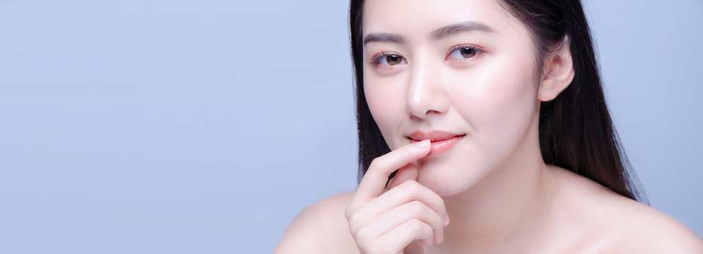 Beauty Face. Beautiful Asian Woman With Natural Makeup And Sexy Full Lips Touching Her Mouth. Closeup Portrait Of Smiling Model Girl With Healthy Smooth Facial Skin Applying Lip Balm On Lip.