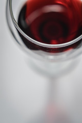 Closeup top view of a glass of red wine with shadows and reflections on a white textured surface.