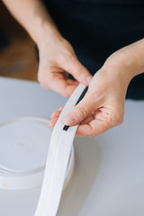 Close-up hands cut with scissors a wide elastic band on thin ribbons. Deficit rubber bands for sewing medical masks. Life hack