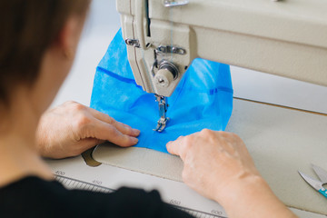 Stepwise stitching of blue fabric medical masks on a sewing machine. A close up of an industrial...
