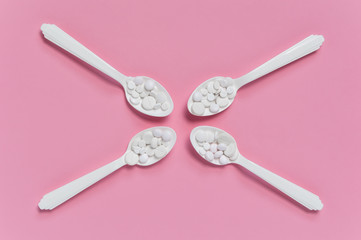 Four spoons with white pills of different size on pink background. Medication dose of prescription drugs for illness therapy. Pharmaceutical or medical flat lay composition