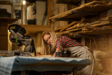 beautiful caucasian skillful carpenter woman measuring piece of wood before cutting it on circular sawer and grinding