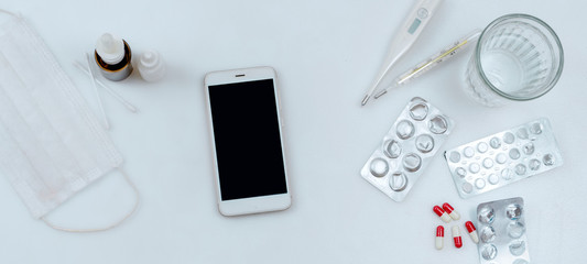 Top view. Pills, glass of water, smartphone and thermometer on white background. Set of medicines.