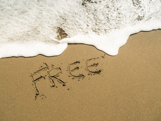 The word FREE written in beach sand with blue ocean water foam in the background 
