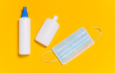 Coronavirus protection. Medical surgical mask and bottles of disinfectant and alcohol hand sanitizer on yellow background. Hygiene measures to prevent spread of Covid-19 pandemic