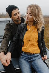 Man sitting on the car hood and looking at the woman who sits on his legs